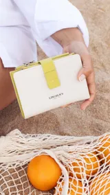 Billetera mediana de símil cuero color blanco hueso con tapa y presilla de cierre en color verde lima. Presenta un monedero con cierre en el borde superior.