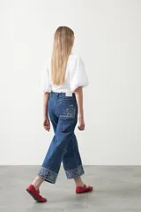 Pantalón de denim azul oscuro con bordado estilo bandana en blanco en los laterales de las piernas y en los puños. El corte es recto y amplio, llegando al tobillo.