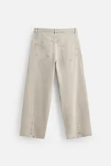 Pantalón de jean color beige, de corte amplio y tiro alto. Tiene cinco bolsillos, cierre frontal con botones y detalle de costuras laterales dobles.