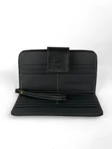 Billetera tipo clutch o cartera de mano, con cuerpo principal de cuero negro texturizado y panel central de pelo (efecto vaca) en tonos blanco y negro. Posee cierre de solapa con broche y correa de muñeca desmontable en cuero negro.