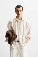 Camisa de hombre regular fit, color blanco con rayas verticales negras, cuello solapa, manga larga con puños abotonados y cierre frontal con botones.