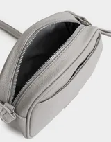 Bandolera negra de cuerina con bolsillo frontal con tag de metal, correa regulable, cierre superior y tirador de material principal.