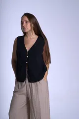 Chaleco tejido color crudo con cuello en V y cierre frontal con tres botones de perlas y lazos decorativos.