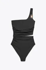 Traje de baño de dos piezas negro, con corpiño asimétrico de un solo hombro con hebilla metálica en el tirante, detalle cut out en el delantero y frunces laterales. La parte inferior es de tiro alto con frunces laterales.