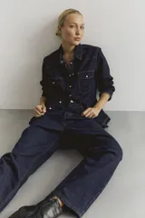Camisa de jean oscuro con cierre frontal y bolsillos en el pecho, de mangas largas.
