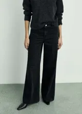 Pantalón de jean negro de corte wide leg, con tiro alto, bolsillos frontales tipo parche y cierre frontal con cremallera y botón.