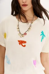 Remera color crudo de corte holgado con mangas cortas rebatidas y bordados de motivos egipcios en hilo de colores.