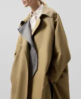 Gabardina larga color beige con interior gris, de tejido a rayas verticales. Tiene mangas largas amplias, cierre frontal cruzado con botones, bolsillos delanteros y aberturas laterales.