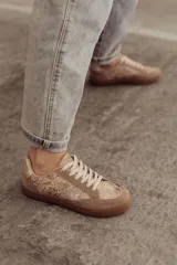 Zapatillas bajas color beige con estampado de piel de serpiente metalizada, cordones blancos y suela color caramelo.