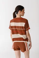 Remera polo tejida a rayas horizontales rojas y rosadas, con cuello clásico y bordado de ají verde.