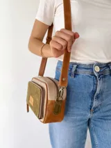 Bandolera rectangular de cuero color beige con frente de gamuza verde oliva y detalles en cuero marrón. Tiene correa larga de cuero marrón regulable y cierre superior con cremallera.