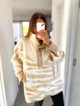 Buzo de poliéster color beige con estampado de leopardo blanco, cuello alto con botones a presión y bolsillos laterales.