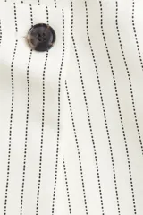 Short pollera mini color blanco con rayas verticales negras, de corte cruzado con botón a la vista y cierre lateral oculto con gancho.