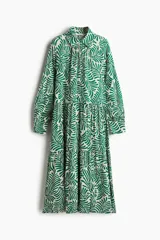 Vestido camisero midi de viscosa con estampado de hojas verdes sobre fondo blanco. Tiene cuello camisero, tapeta de botones oculta, mangas largas raglán con puños sencillos y costuras fruncidas en la falda.