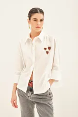 Camisa blanca de algodón con bordados de corazones rojos y dorados en el delantero. Tiene cartera en el delantero y fruncido en el centro de la espalda.