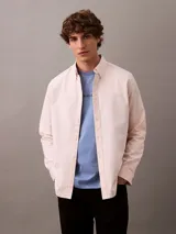 Camisa de manga larga color rosa claro, confeccionada en tejido Oxford de algodón y elastano. Presenta cuello camisero clásico, cierre frontal con botones y logo de Calvin Klein bordado en el pecho. Corte regular.