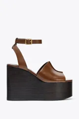 Sandalias de cuero color marrón con plataforma de cuña de madera oscura y correa de tobillo ajustable con hebilla dorada.