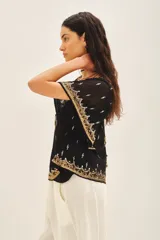 Blusa de gasa traslúcida negra con escote en V y mangas amplias de largo irregular, bordada con canutillos, lentejuelas y mostacillas doradas. Incluye gancho oculto en el escote y viso al tono con breteles regulables y puntilla en el escote.