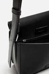 Bandolera negra con textura grabada, compartimento principal con cierre de solapa imantada, bolsillo interior con cierre y asa de hombro ajustable.