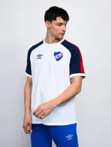 Remera de algodón azul con mangas ranglan azul marino y detalles en blanco en cuello y puños. Incluye logo de Umbro y escudo del Club Nacional de Football en el frente.