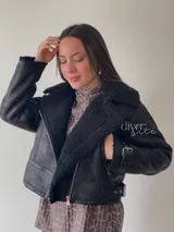 Campera gamulán negra con interior de corderito sintético, cierre cruzado con cremallera y hebilla en el ruedo.