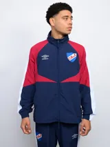 Campera deportiva Umbro del Club Nacional de Football, con diseño color block en azul marino, rojo y blanco. Incluye cierre frontal, cuello alto, bolsillos laterales y escudo del club bordado en el pecho.