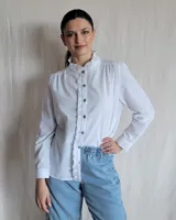 Camisa blanca de manga larga con cuello alto con volados y botones marrones.