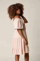 Vestido corto blanco con escote bardot, cintura fruncida y falda escalonada con vuelo.