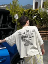 Remera celeste con estampa de paisaje costero y texto "Ittai Stars" y nombres de ciudades.