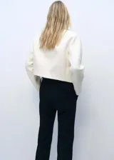 Chaqueta corta color crema con cuello redondo y detalles troquelados.