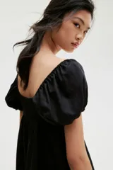 Vestido corto negro con escote corazón, mangas cortas abullonadas con elástico en hombros y puños, espalda fruncida y falda con vuelo.