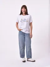 Remera blanca de algodón con cuello redondo y manga corta. Presenta un pequeño bordado en el pecho izquierdo con una figura que parece ser una persona acostada en una tabla de surf o flotador.