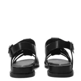 Sandalias planas de cuero negro, estilo pescador o gladiadora, con tiras anchas entrelazadas en la parte delantera y cierre ajustable con hebilla metálica en el tobillo.