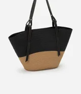 Bolso de playa grande de paja bicolor, negro en la parte superior y beige en la inferior, con asas de cuero sintético negro.