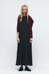 Vestido midi negro de cuello redondo y sin mangas. Corte amplio y fluido, con bolsillos laterales ocultos y cierre trasero con cremallera invisible.