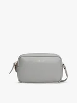 Cartera bandolera rectangular de cuero sintético color gris claro, con cierre superior de cremallera y logo metálico de Tommy Hilfiger en el frente.