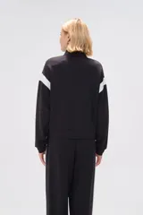 Campera deportiva negra con cierre frontal, cuello alto y detalles de recortes curvos blancos en mangas y laterales.