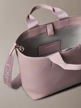 Mini cartera tote Calvin Klein color rosado, confeccionada en poliuretano con doble asa de mano y correa de hombro ajustable extraíble. Incluye cierre con botón a presión y bolsillo interior para tarjeta.