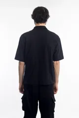 Remera polo negra de manga corta con cierre dorado en el cuello y logo bordado en el pecho.