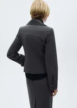 Chaqueta gris con finas rayas verticales, corte entallado, cuello camisero, cierre frontal con cremallera doble, bolsillo de ribete en el pecho y mangas largas.