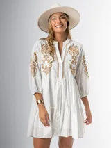 Vestido corto blanco de algodón italiano con bordado azul, mangas tres cuartos y botones frontales.
