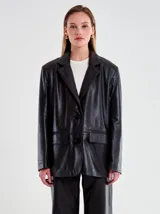 Chaqueta tipo blazer oversize de cuero sintético negro, con solapas de muesca, cierre frontal de dos botones y dos bolsillos de parche frontales.