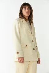 Abrigo de cuello sastre color beige, con forro, cierre frontal con botones, bolsillos con solapa y presillas en mangas. Confeccionado en lana fina sin teñir, diseñado exclusivamente por Don Baez.