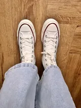Zapatillas de lona blancas de caña alta con cordones y puntera de goma. Logo de durazno engomado en la base y en la cara interna.