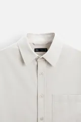 Camisa color crema de corte relaxed fit, confeccionada en tejido de mezcla de algodón suave al tacto. Tiene cuello solapa, manga larga con puños abotonados, un bolsillo de parche en el pecho y cierre frontal con botones.