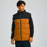 Chaleco acolchado Caterpillar, color marrón con parte superior negra, cierre frontal con cremallera, cuello alto y bolsillos laterales con cierre.