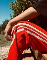 Pantalón de jogging rojo con tres rayas blancas verticales en los laterales.