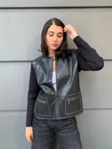 Campera negra con cuerpo de cuero sintético y mangas largas de tejido de punto fino. Presenta cierre frontal con cremallera, cuello redondo y bolsillos con cierre en el frente. Detalles de costuras en color blanco.