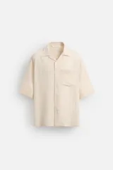Camisa color crema de manga corta con cuello bowling, corte relaxed fit y bolsillo de parche en el pecho.