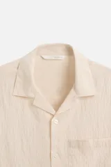 Camisa color crema de manga corta con cuello bowling, corte relaxed fit y bolsillo de parche en el pecho.